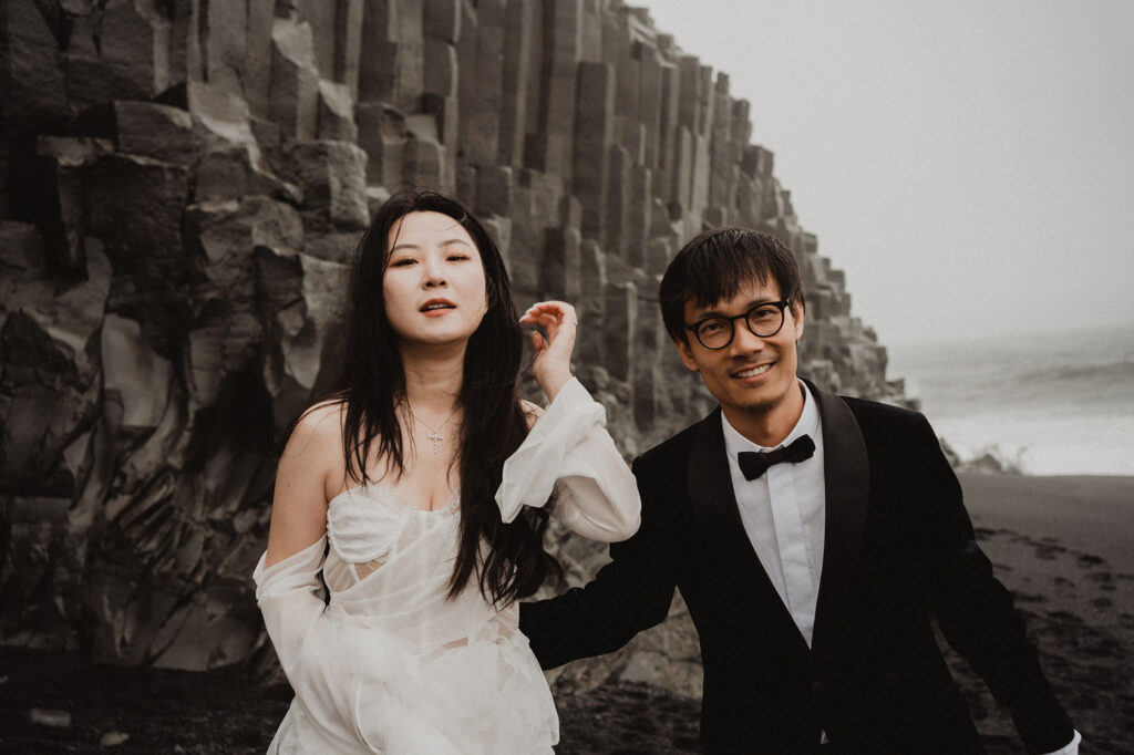 bride and groom sit on rock formations on diamond beach during iceland wedding photo shoot.