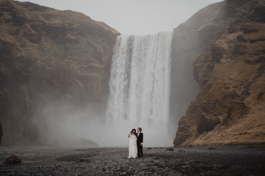 bride and groom stand in front of waterfall during iceland adventure elopement.
