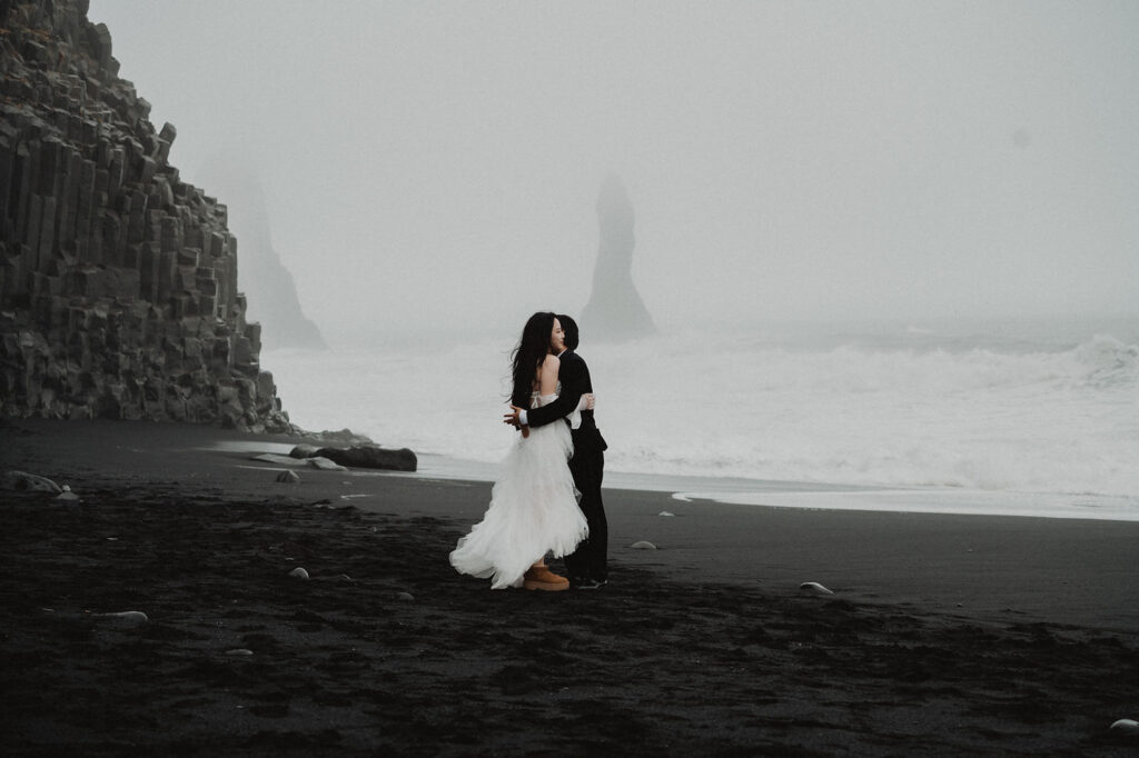 bride and groom hug on black beach in iceland during adventure wedding photos.