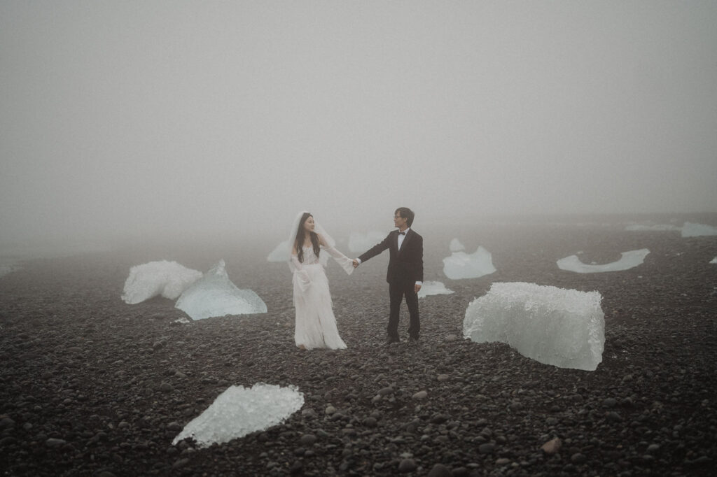 newlywed couple stands and holds hands on diamond beach in iceland during wedding portraits.