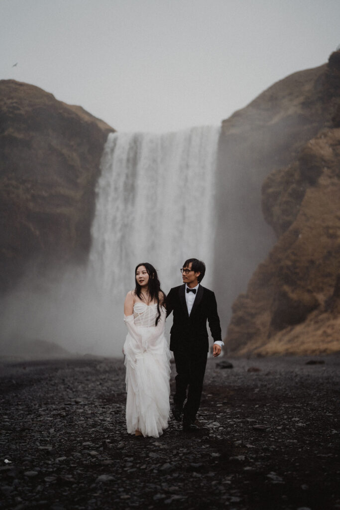 bride and groom stand in front of waterfall during iceland wedding.