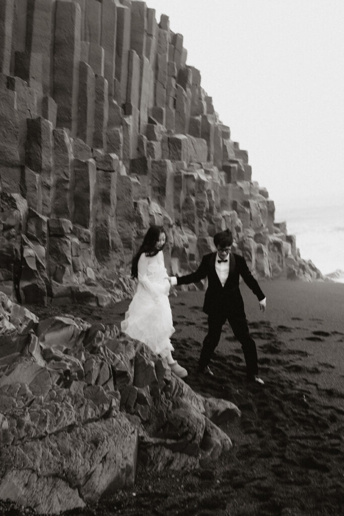 black and white image of couple stepping off rock formations during iceland elopement.