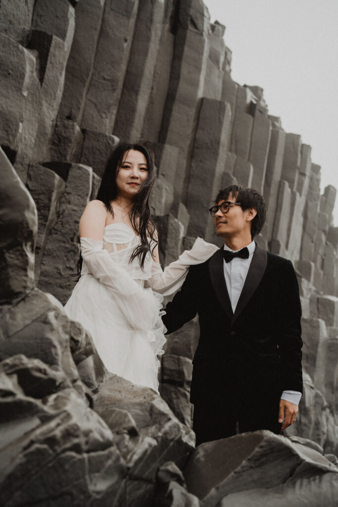 bride and groom stand on rock formation on iceland coast during iceland wedding photo shoot.