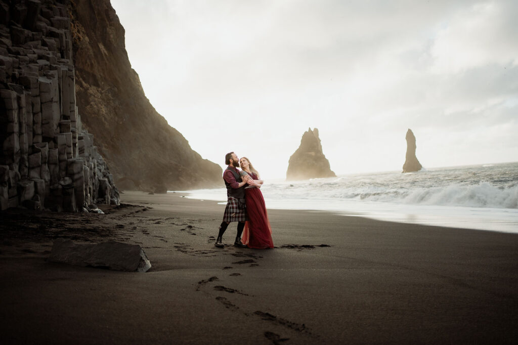 A man holds a woman in front of her on Reynisfjara beach during honeymoon pictures with Iceland Wedding Photographer.