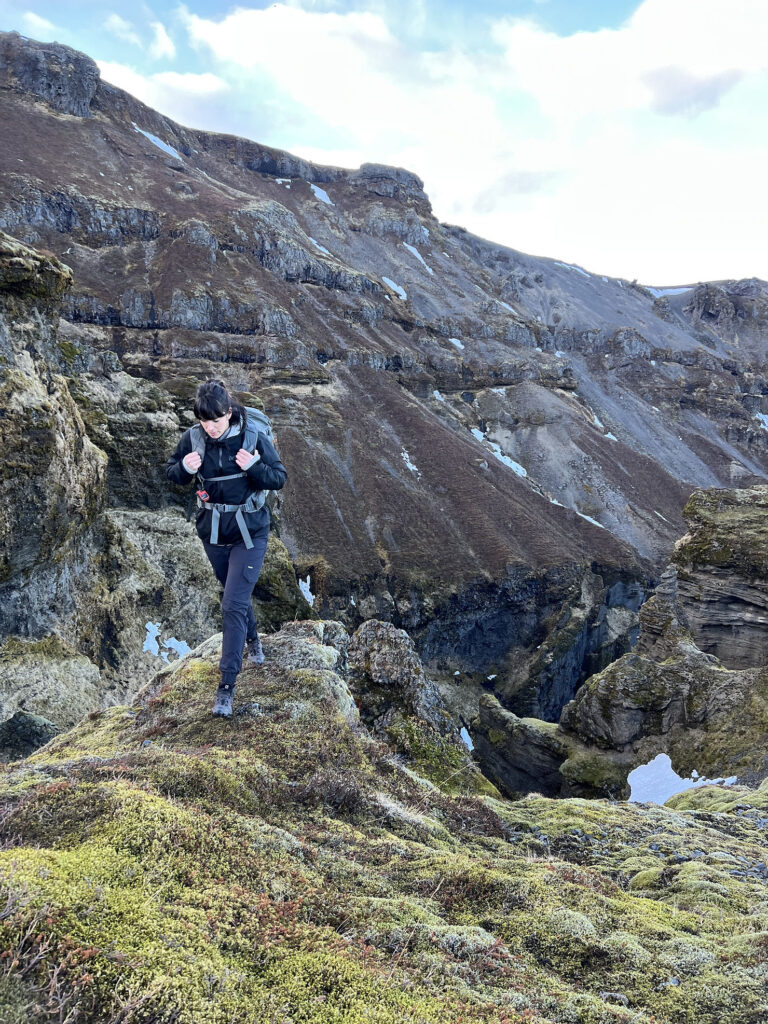 Iceland Wedding Photographer takes photos during a hike in Iceland with her family.  She is hiking on the edge of a valley with small daughter in backpack carrier.