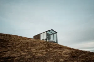 glass cabin sits on a hill in iceland