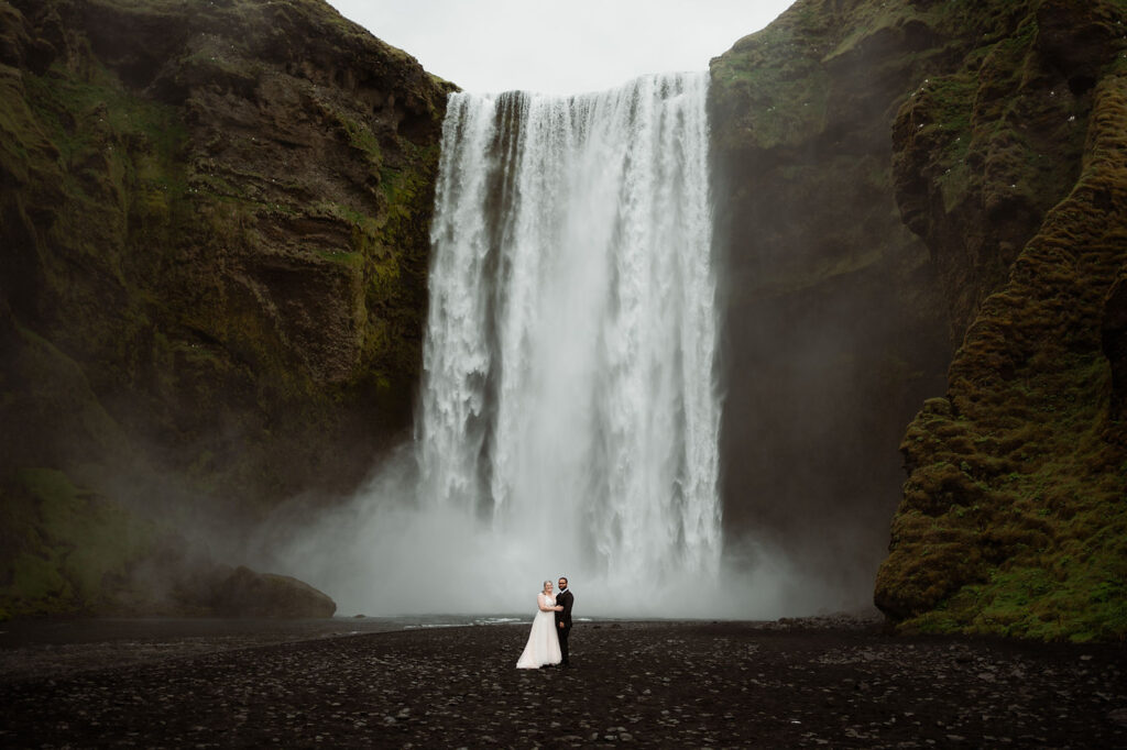 How to Include Your Family When You Elope: Bride and groom stand in front of a large waterfall amidst mossy cliffs.