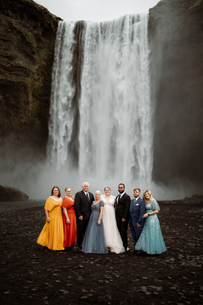 How to Include Your Family When You Elope: A group in formal attire poses happily in front of a large waterfall.