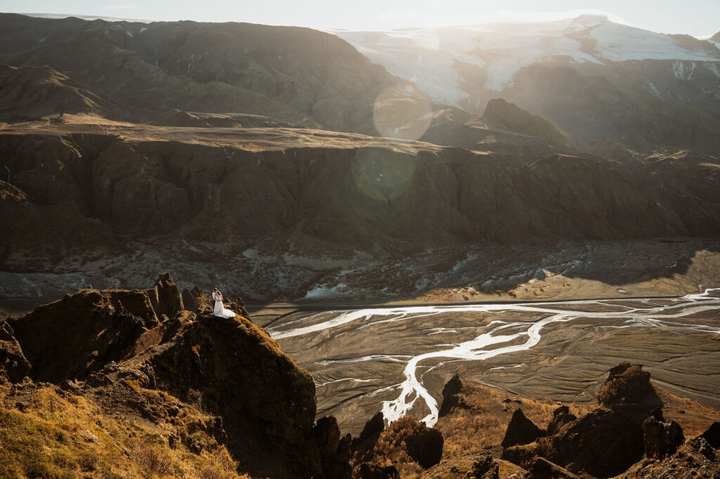 Bride and groom stand on a rocky cliff at Þórsmörk Valley, overlooking a vast, rugged landscape during elopement.