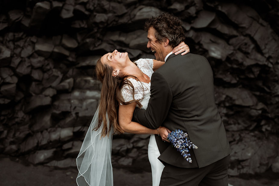 newlywed couple laughs under rock formation during adventure iceland wedding.