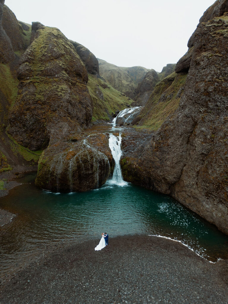bride and groom stand at the base of a waterfall during iceland wedding day.